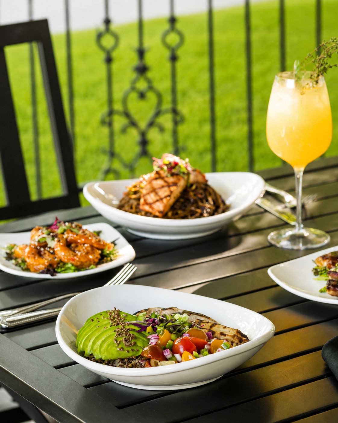A table with various dishes, including a salad with avocado and a bowl of noodles topped with meat.