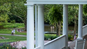 A covered outdoor area with white columns, a pathway, and a pond with two people fishing. - Allenberry Resort (Boiling Springs)