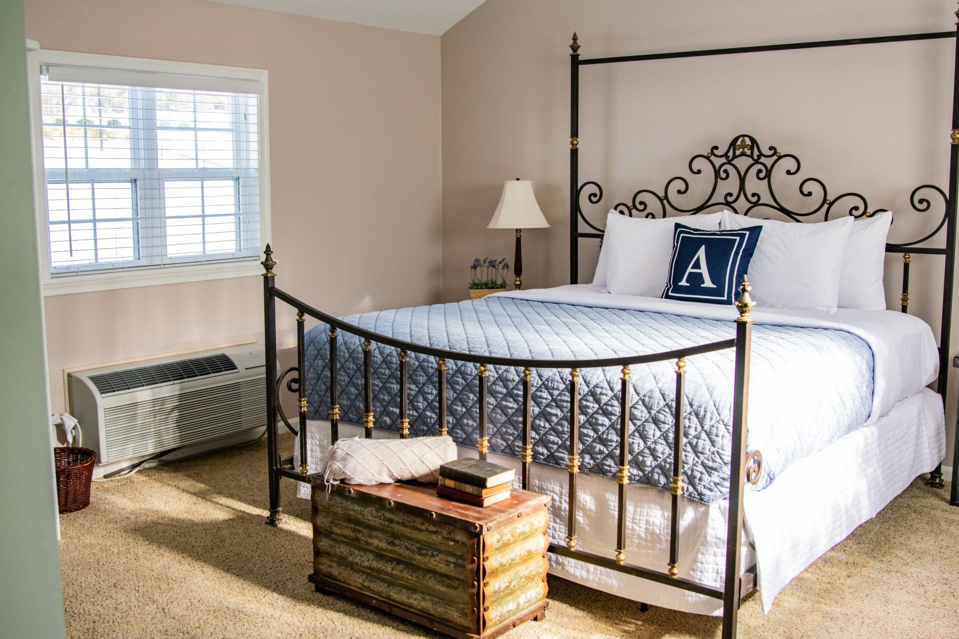 A bedroom with a four-poster bed, a bedside lamp, a window with blinds, and a radiator.