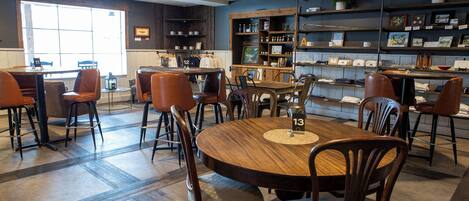 Un restaurant doté d’une grande table ronde au centre, de plusieurs tabourets de bar et d’un espace salon avec des chaises.