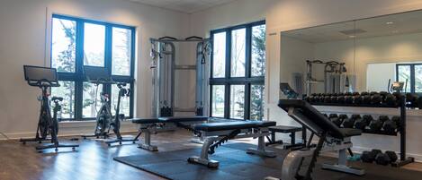 A gym with exercise equipment, large windows, and a mirror.