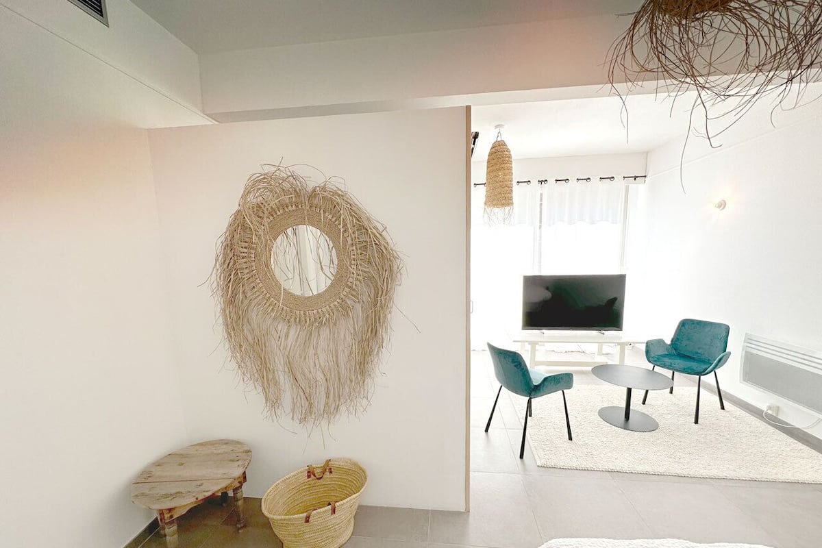 A modern living room with a large TV, teal chairs, a round coffee table, and a woven wall decoration.