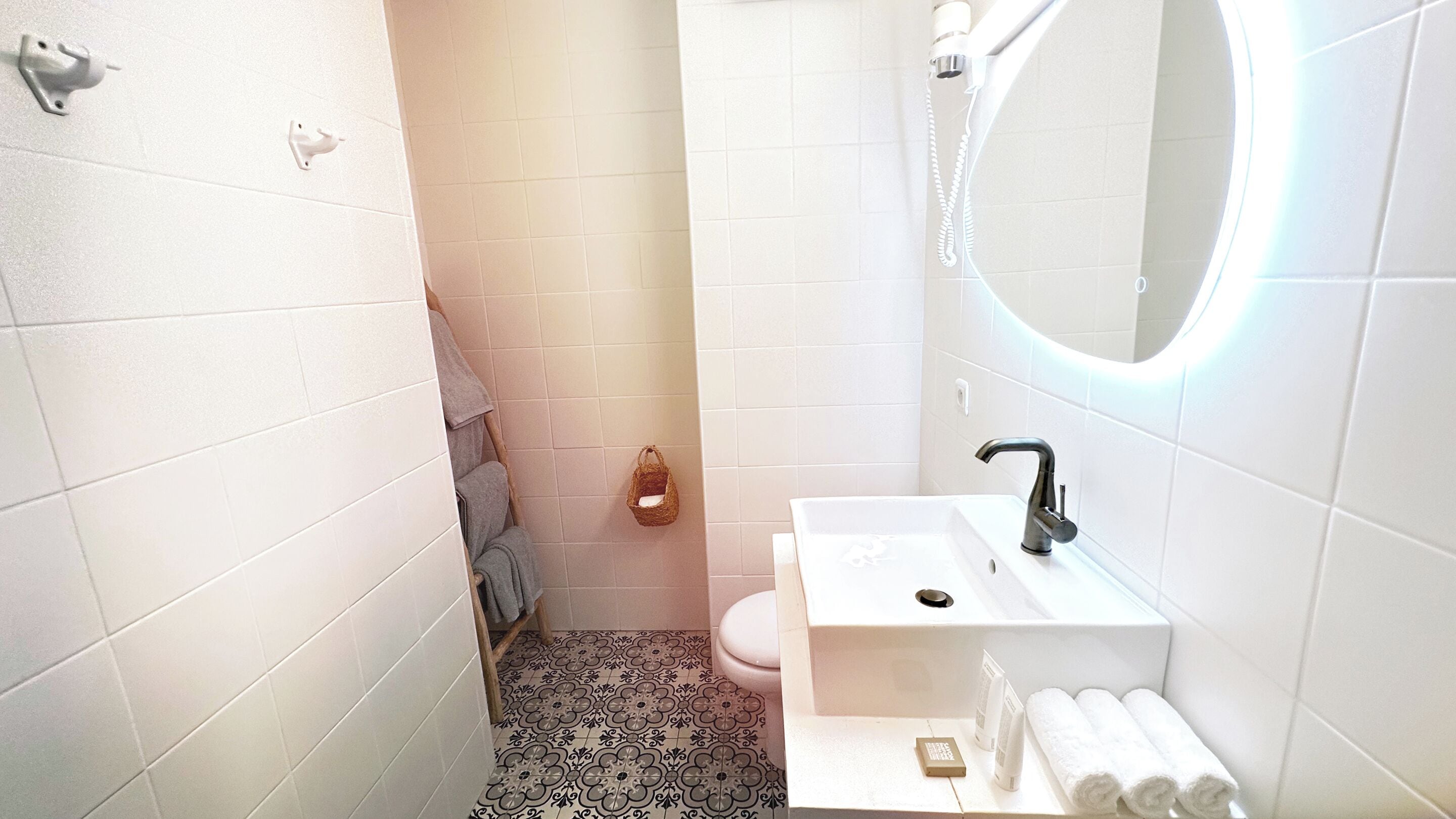 Ein kleines Badezimmer mit weißen Fliesen, einem Waschbecken, einer Toilette und einem Spiegel.