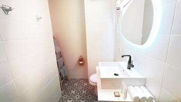 Ein kleines Badezimmer mit weißen Fliesen, einem Waschbecken, einer Toilette und einem Spiegel.