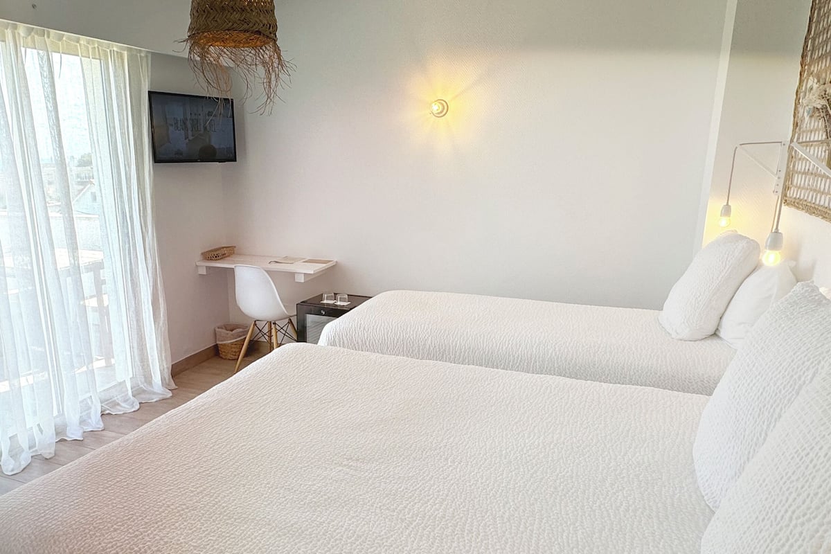 A bedroom with two beds, a desk, a chair, and a TV on the wall.