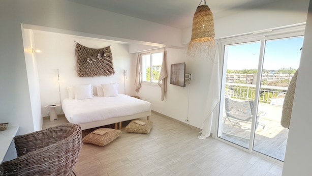 Ein modernes Schlafzimmer mit einem großen Bett, einem Korbstuhl, einer Pendelleuchte und einer Glasschiebetür, die auf einen Balkon führt.