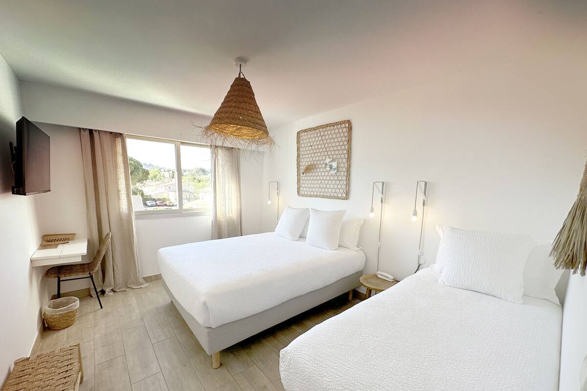 A hotel room with two beds, a desk, a chair, a TV, and a window with curtains.