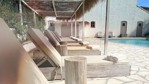 Ein Poolbereich mit Liegestühlen und Handtüchern, einem Reetdach und einem Steineinfassung.