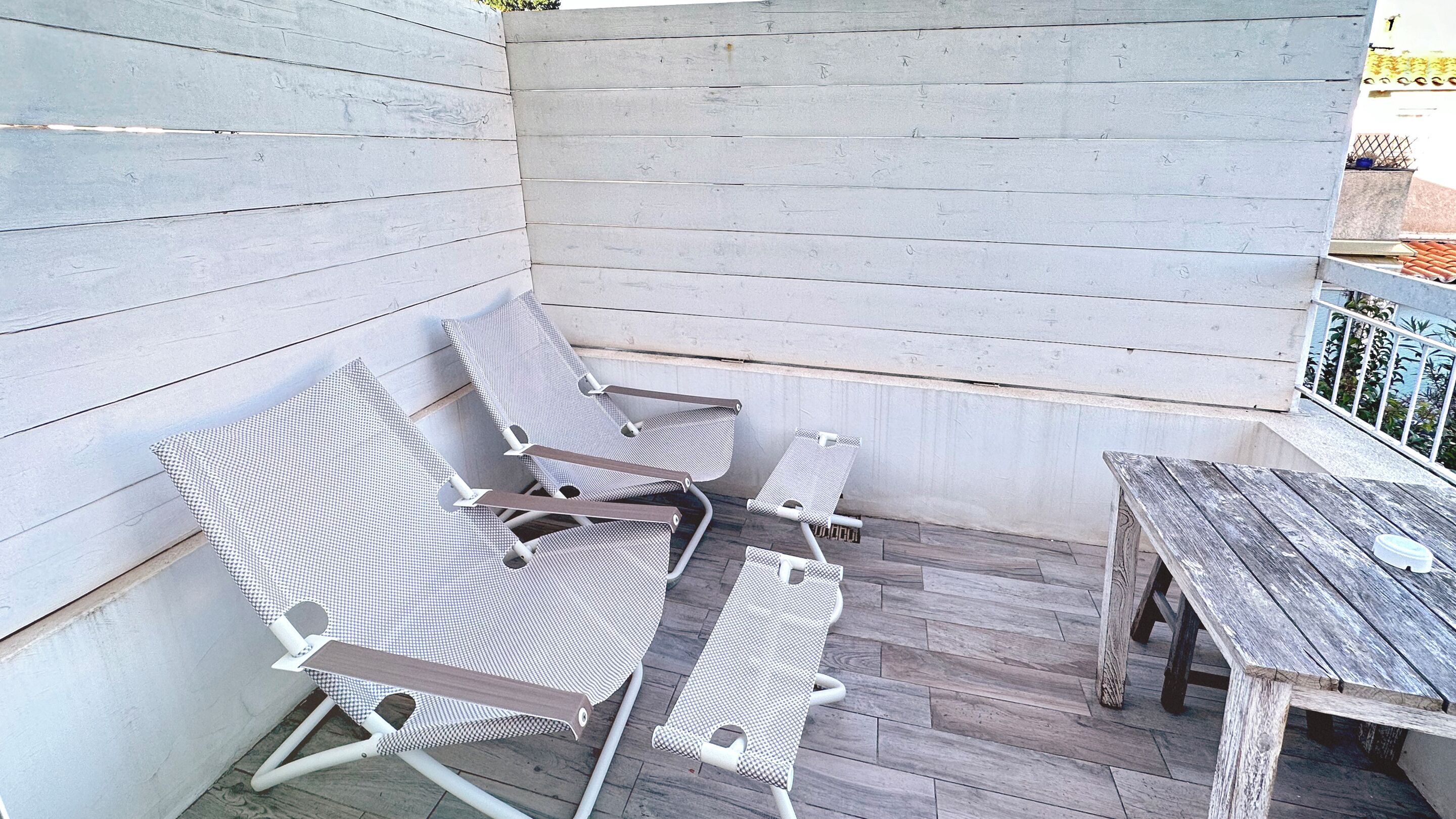 A balcony with wooden flooring, white walls, and a wooden table.