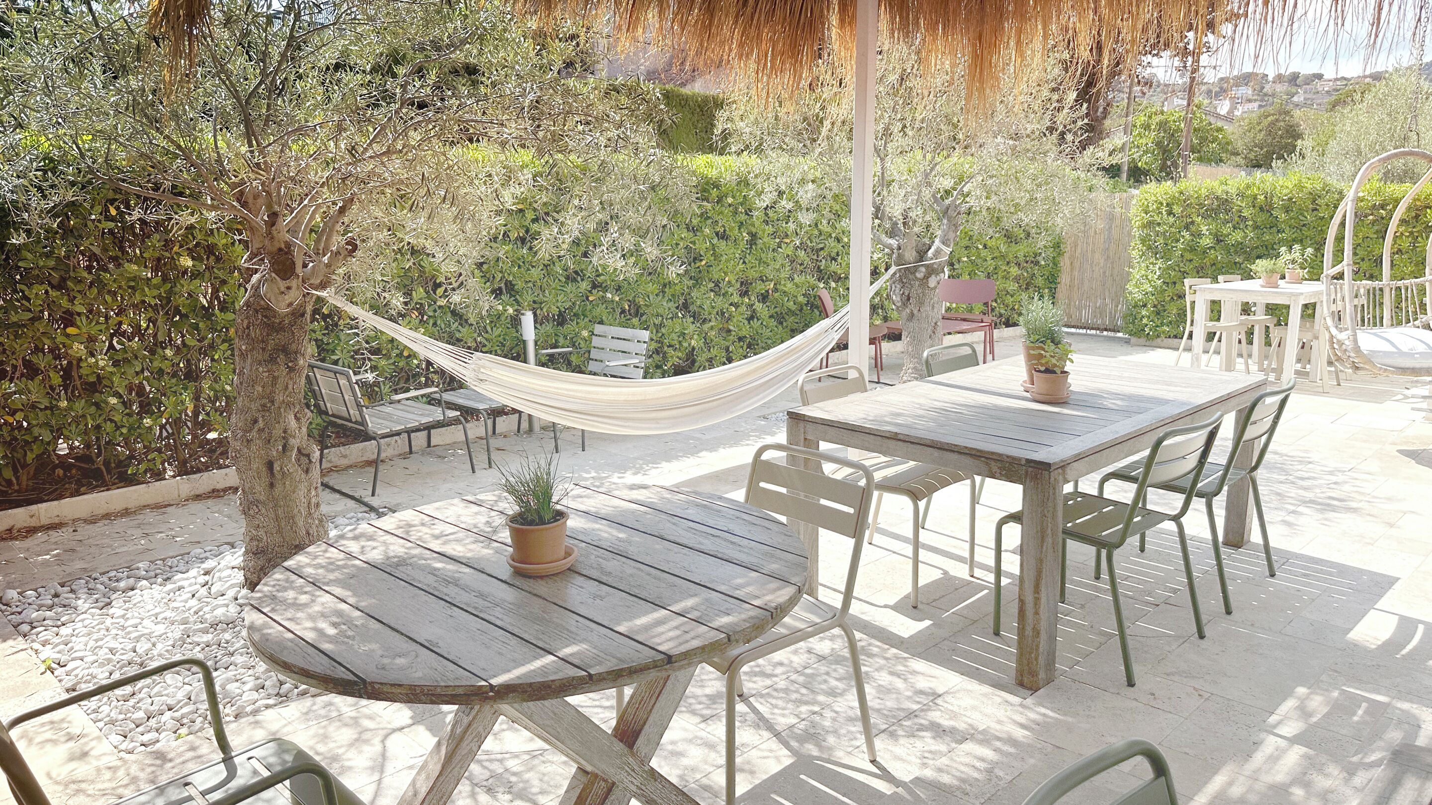 Une terrasse extérieure avec une table et des chaises en bois, un hamac et des plantes en pot.