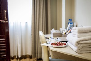 Une chambre d’hôtel avec un bureau en bois, un bol de fraises, une pile de serviettes blanches, une bouteille d’eau et une boîte de mouchoirs.