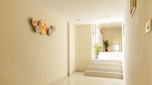 Un pasillo limpio y moderno con una escalera que conduce a un nivel superior. Se observan placas decorativas en la pared y una planta en maceta en la escalera.