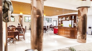 Un vestíbulo amplio con techos altos, grandes columnas de cobre, un mostrador de recepción y sillas de madera.