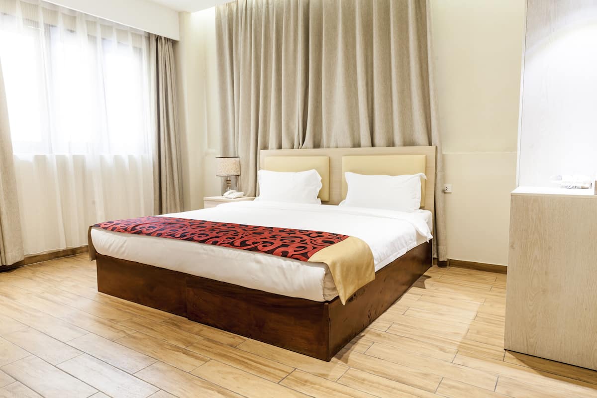 A hotel room with a large bed, a wooden headboard, a bedside table with a lamp, and a wardrobe.