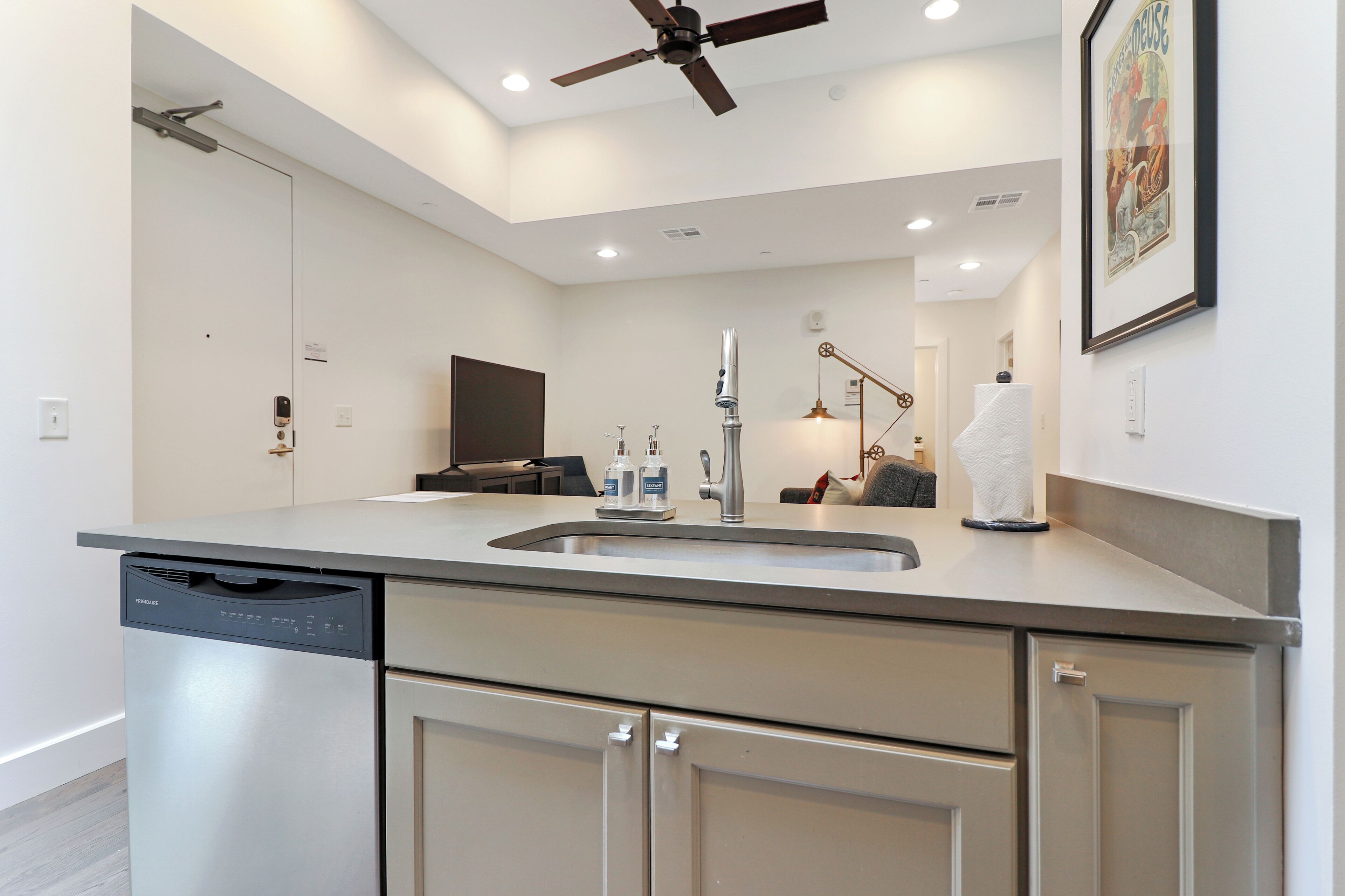 Una cucina moderna con lavastoviglie, mobili in acciaio inossidabile, lavello integrato e ventilatore a soffitto.