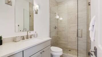 A modern bathroom with a glass-enclosed shower, a white sink, and a toilet.