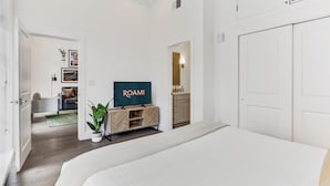 Una camera d'albergo moderna con un letto grande, una TV su un supporto in legno, una pianta in vaso e vista sull'area soggiorno.