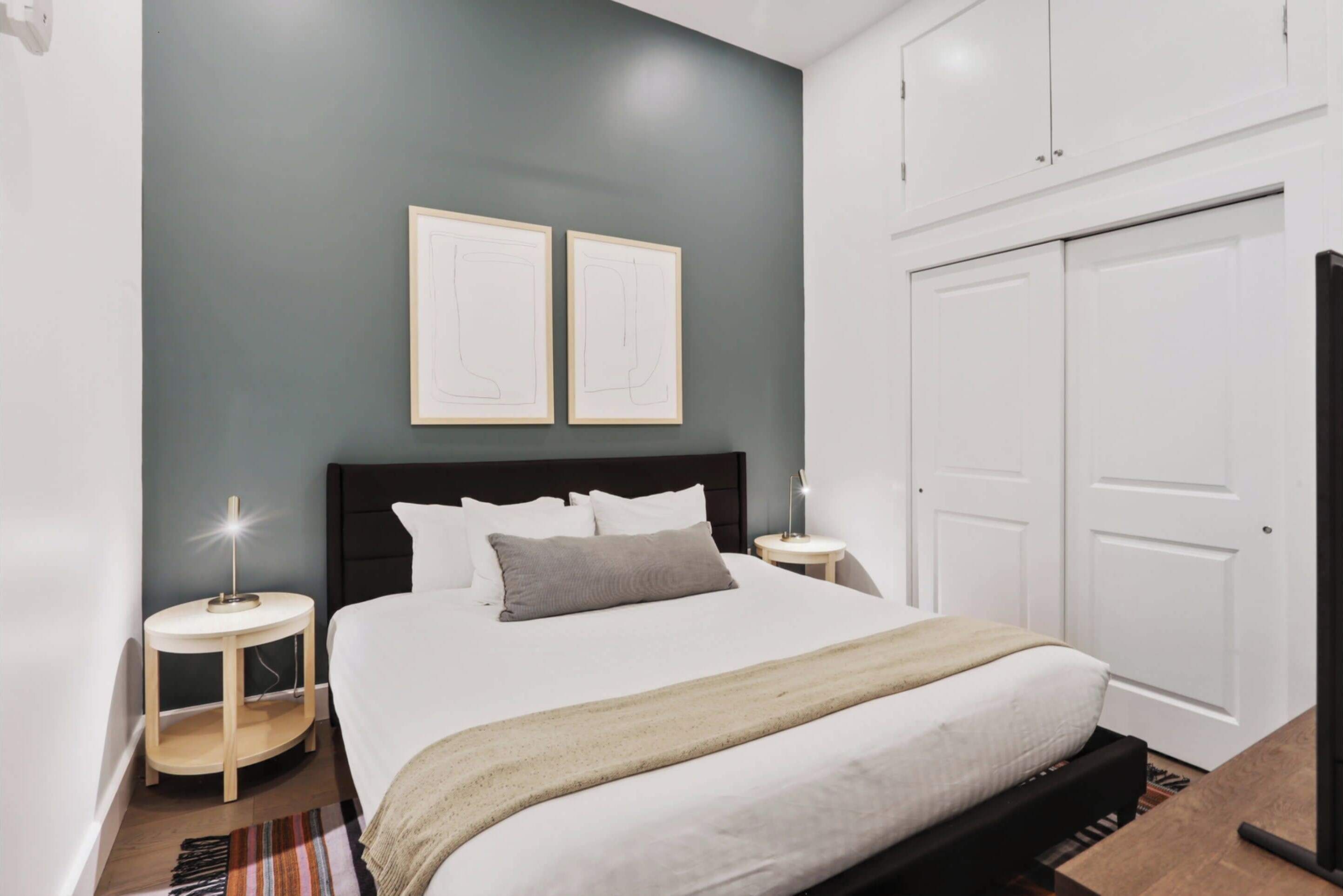 Un dormitorio con una cama, dos mesitas de noche, un aparador, y dos cuadros en la pared.