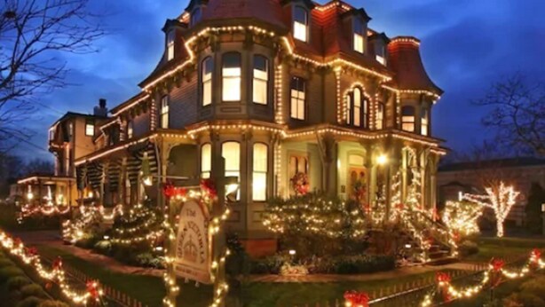 A large, historic house with multiple windows and a prominent front porch, decorated with lights and greenery. - The Queen Victoria B&B (Cape May)
