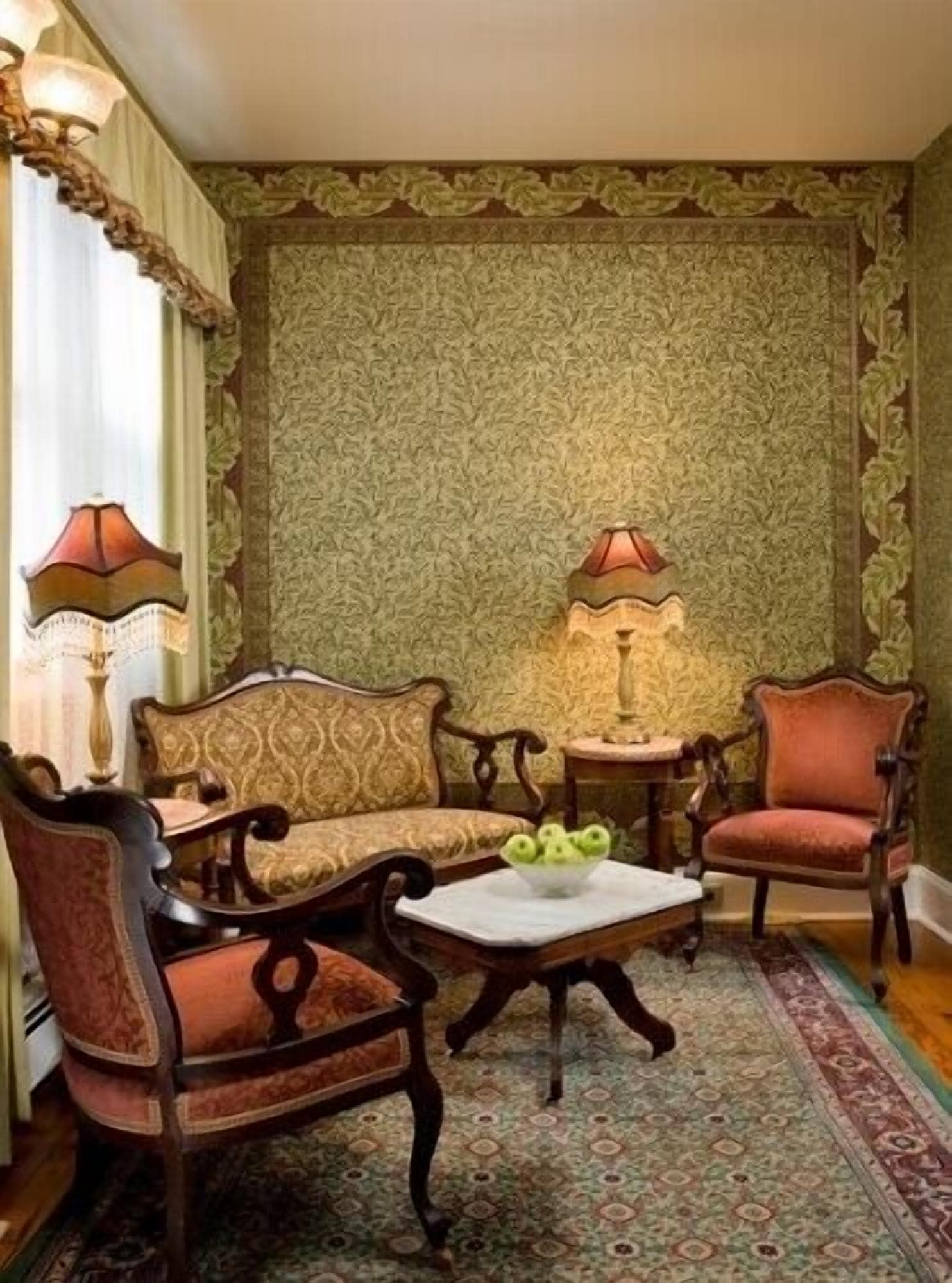 Una habitación tradicional con papel tapiz estampado, un sofá, dos sillones, una mesita con una lámpara y un cuenco decorativo sobre la mesa.