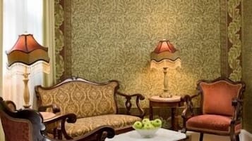 Una habitación tradicional con papel tapiz estampado, un sofá, dos sillones, una mesita con una lámpara y un cuenco decorativo sobre la mesa.