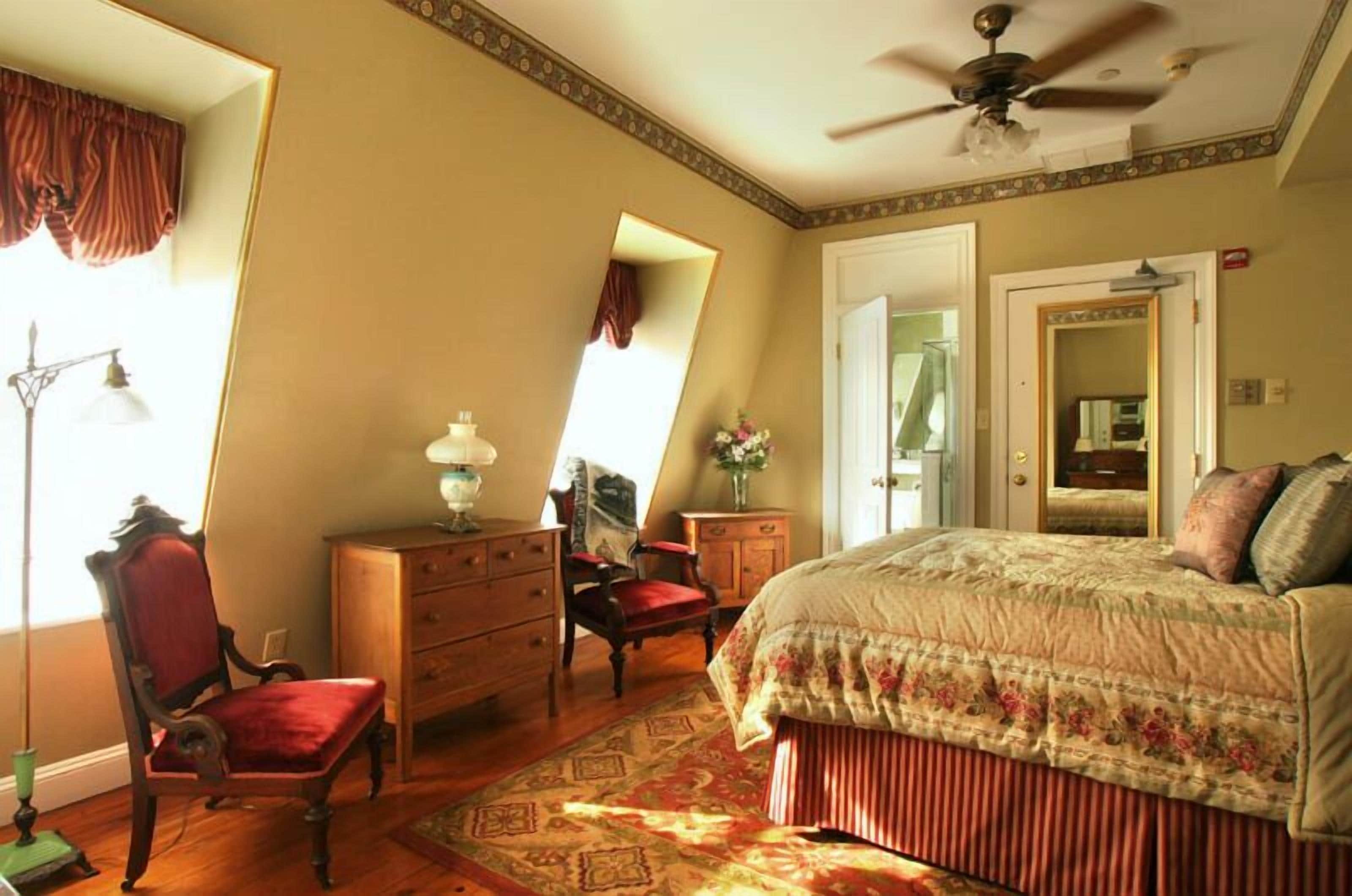 A bedroom with a bed, a dresser, a chair, a mirror, and a ceiling fan.