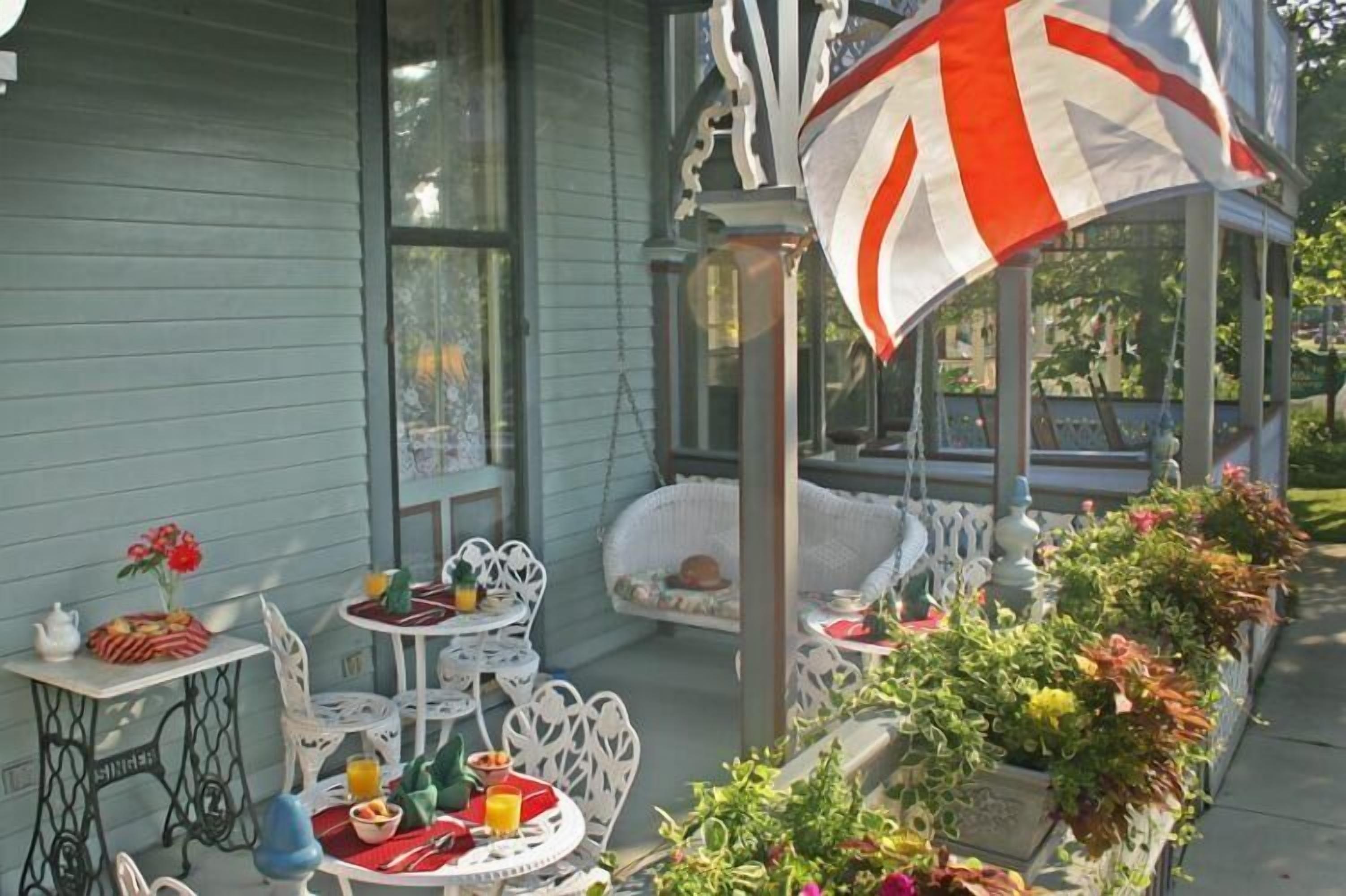 A patio with white wicker furniture, a table with a red and white striped umbrella, and a garden with flowers.