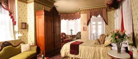 A traditional room with a bed, a sofa, a wooden wardrobe, a small table, and a window with curtains.