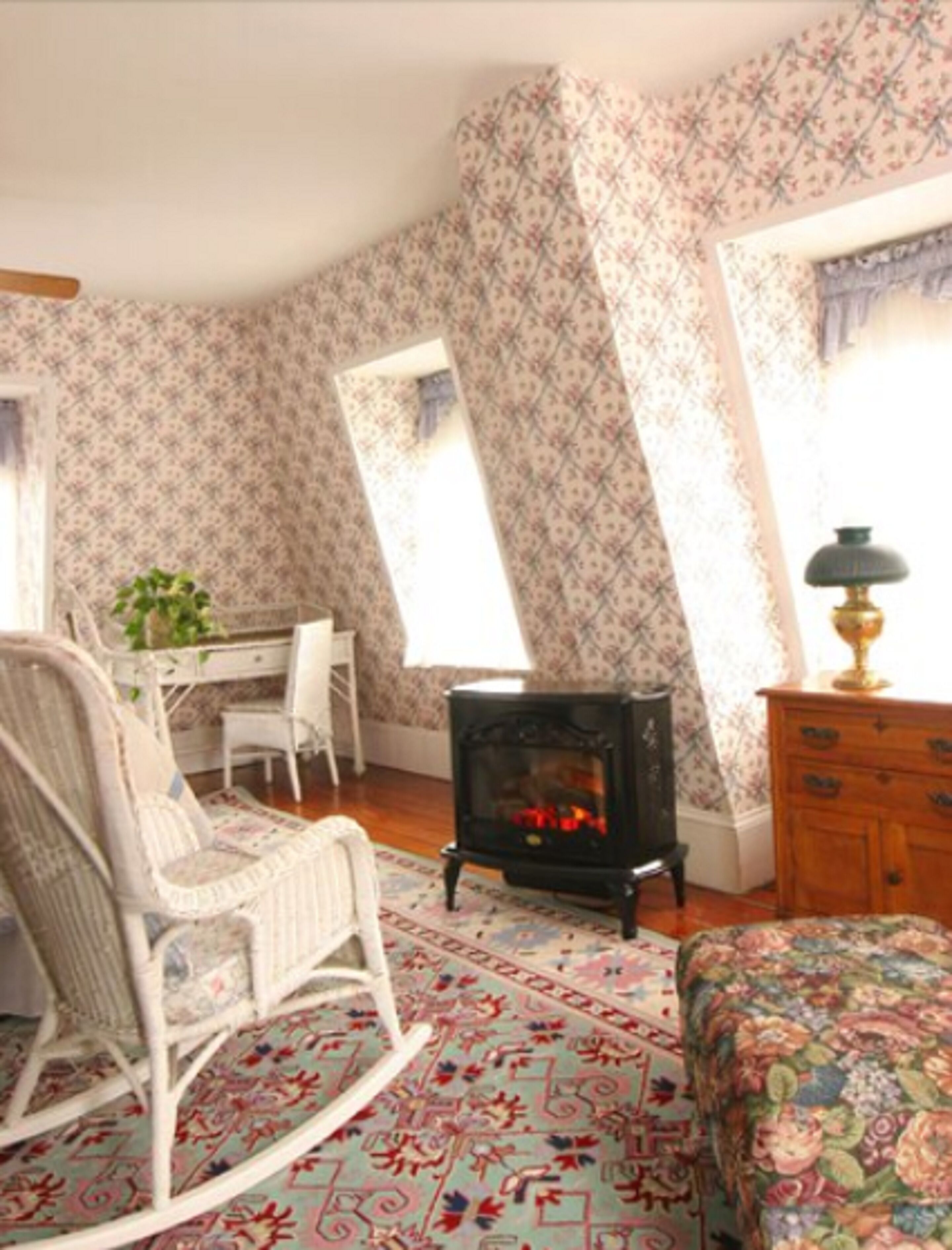 A cozy room with a rocking chair, a desk, a fireplace, and a bed.