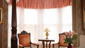 A traditional room with a four-poster bed, two chairs, a table with a lamp, and a vase of flowers.