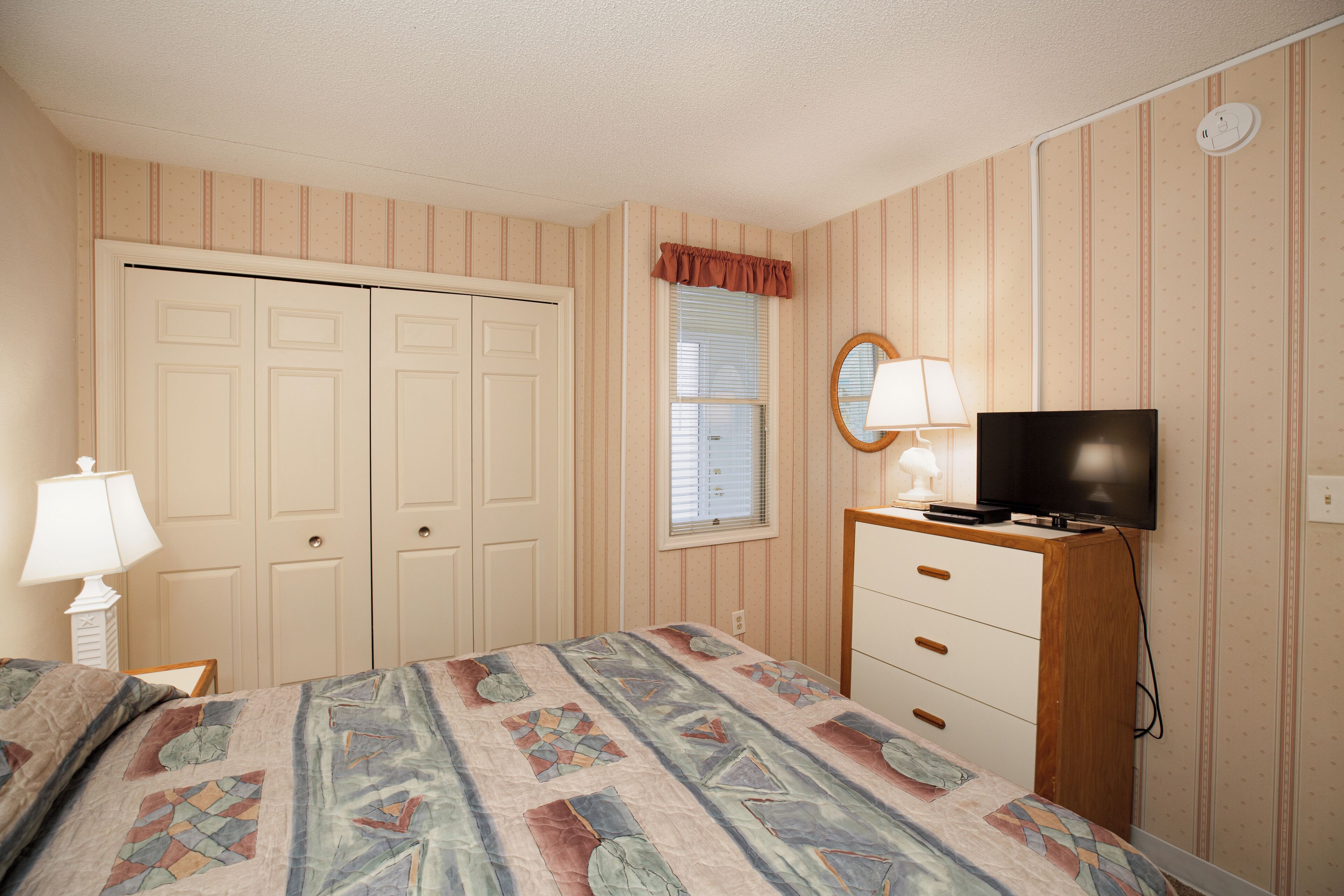 A bedroom with a bed, a dresser, a television, and a window with blinds.