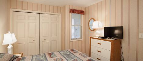 A bedroom with a bed, a dresser, a television, and a window with blinds.
