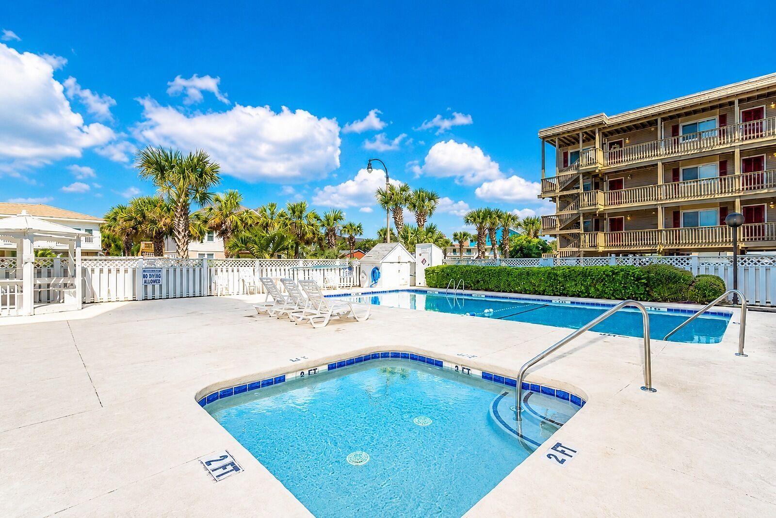A hotel pool area with a hot tub, lounge chairs, and a multi-story building in the background.