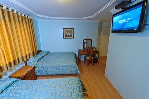 Habitación de hotel con dos camas, un escritorio, una silla, un televisor y una ventana con cortinas.