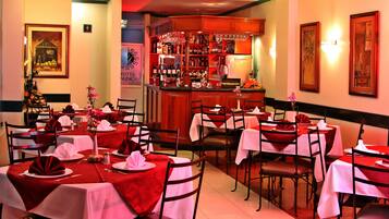 A restaurant with tables set for dining, a bar area with bottles and glasses, and framed artwork on the walls.