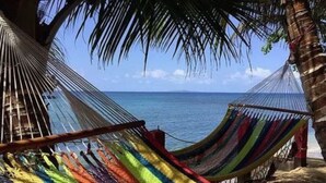 Una hamaca con tela a rayas de colores, frente a un cielo azul despejado y un mar tranquilo, con palmeras enmarcando la escena.