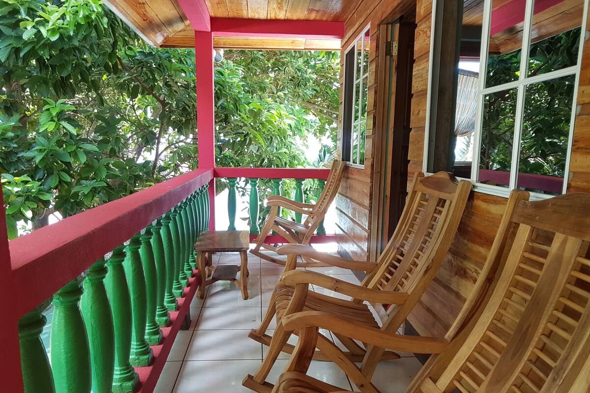 Une véranda en bois avec une balustrade rouge, des poteaux verts et des fauteuils à bascule en bois.