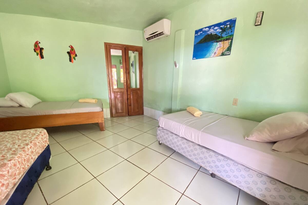 Une chambre avec deux lits simples, une porte en bois, un climatiseur mural et un tableau sur le thème de la plage.
