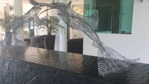 Eine Skulptur verschlungener Figuren auf einer Marmorplatte in einem Eingangsbereich mit modernem Design, einschließlich einer Glastrennwand und einem Topfpflanzen.