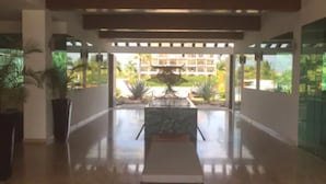 Eine großzügige Lobby mit einem zentralen Wasserspiel, Topfpflanzen und Blick auf ein Gebäude im Hintergrund.