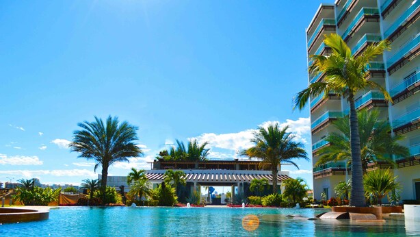 Ein Hotel mit Pool, Palmen und einem mehrstöckigen Gebäude mit Balkonen.
