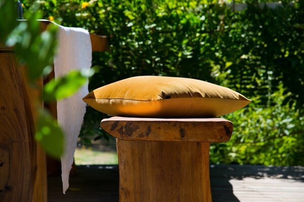 A wooden stool with a cushion on top, set against a backdrop of greenery. - Mahala 2 (Daylesford)