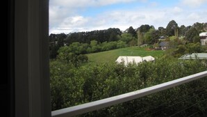 A view from a window overlooking a green landscape with trees and a few buildings in the distance. - Marzden Cottage (Daylesford)