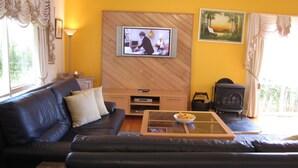 A living room with a sofa, a television mounted on a wooden wall, a table with a bowl, and a fireplace. - Marzden Cottage (Daylesford)
