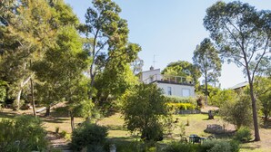 A house surrounded by a well-maintained garden with a variety of plants and a stone pathway leading to the entrance. - Monigatti (Hepburn Springs)