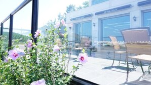 A modern hotel with large windows, outdoor seating, and a view of a bridge. - Pinebeach Hotel Pohang (Pohang)