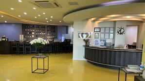 A reception area with a curved counter, a desk with chairs, a display of wine bottles, and a vase with white flowers. - Pinebeach Hotel Pohang (Pohang)