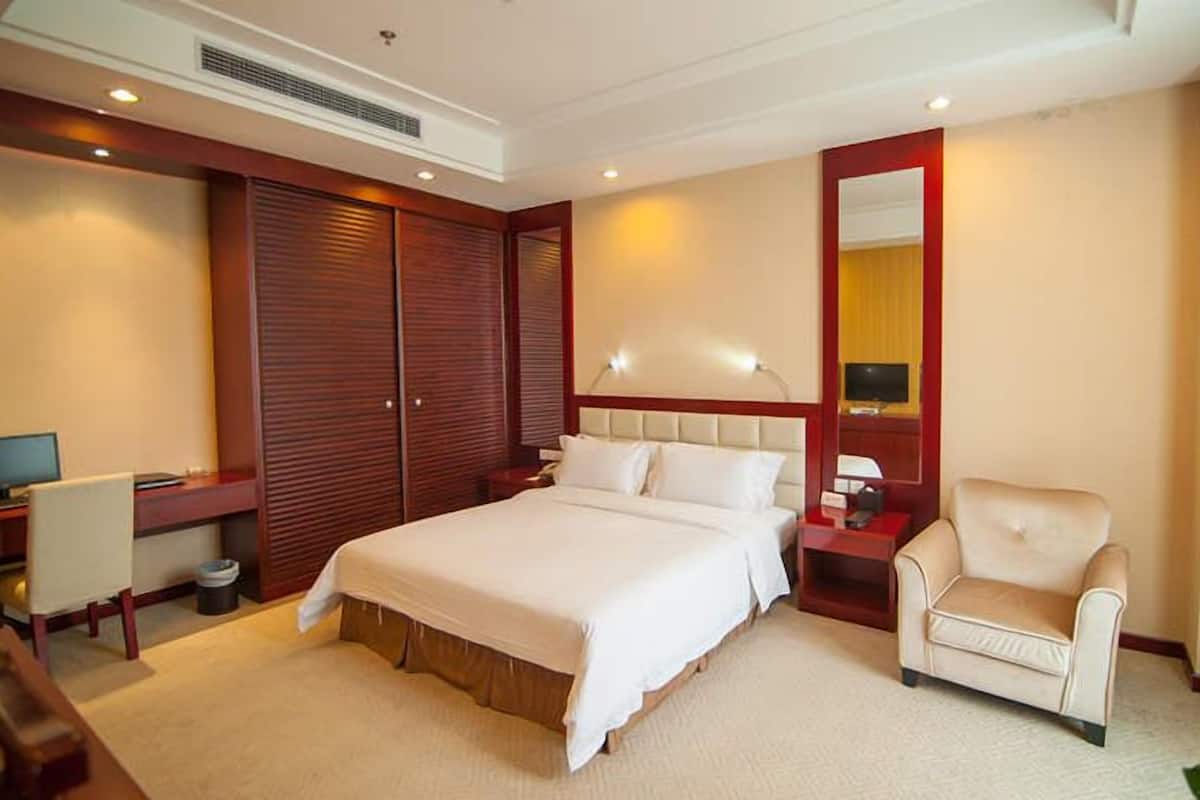 Quarto de hotel com uma cama grande, uma escrivaninha com computador, uma cadeira e uma televisão.