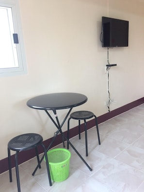 Una habitación pequeña con una mesa, dos sillas, una cesta verde y un televisor montado en la pared.