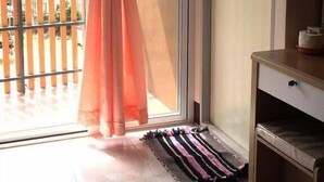 Un balcón con puerta corredera de vidrio, barandilla de madera y un tapete a rayas en el suelo.
